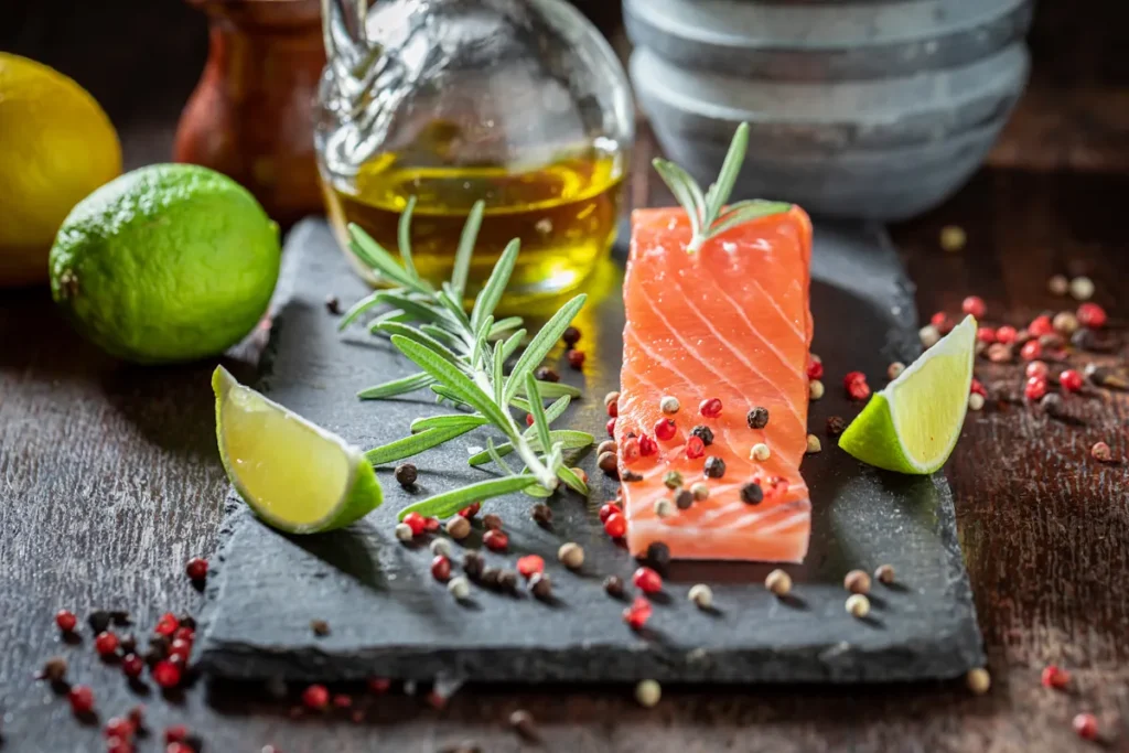 Une tranche de poisson posé sur un support en ardoise à côté de citron, d'huile et de quelques graines