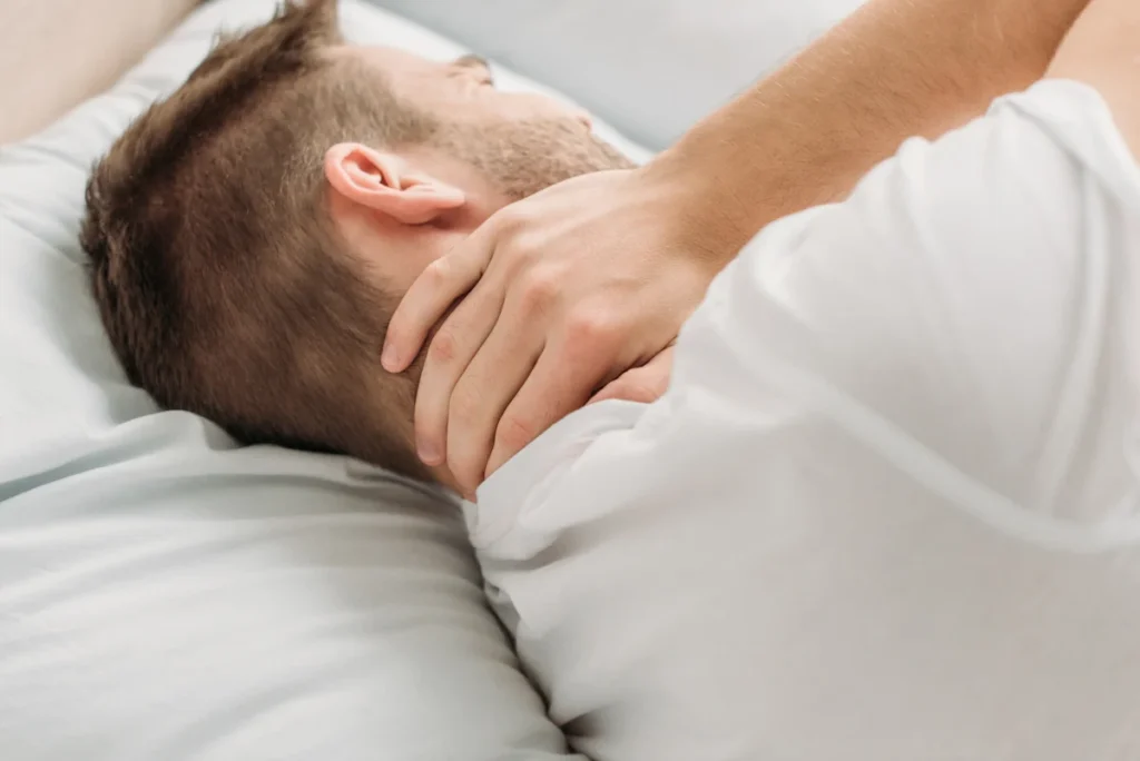 Un homme qui dort sur le côté en se tenant le cou