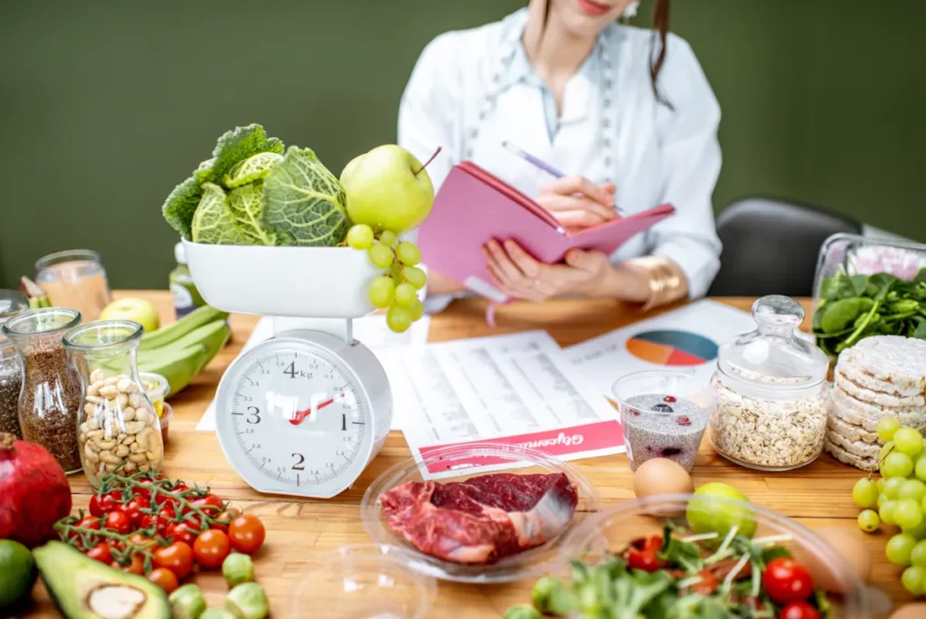 Une nutritionniste qui fait des calculs entourés de plusieurs légumes et documents