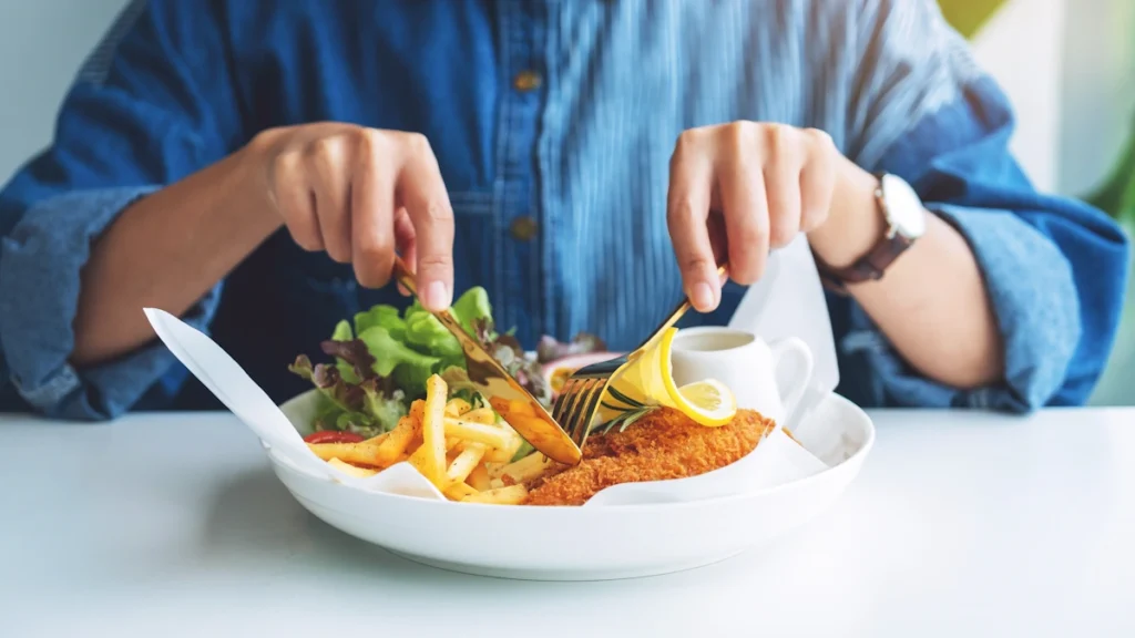 Un homme qui mange une assiette de poisson panné avec des frites et une salade