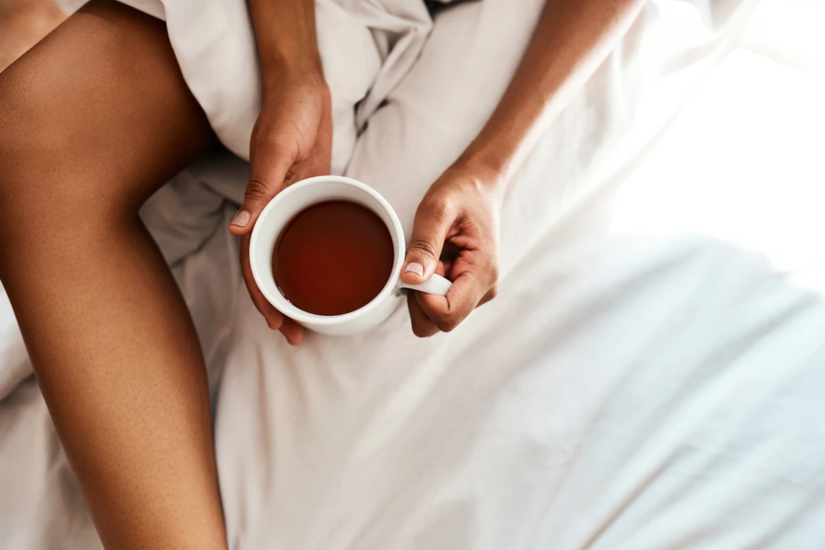 Une personne qui tient une tasse de thé dans un lit
